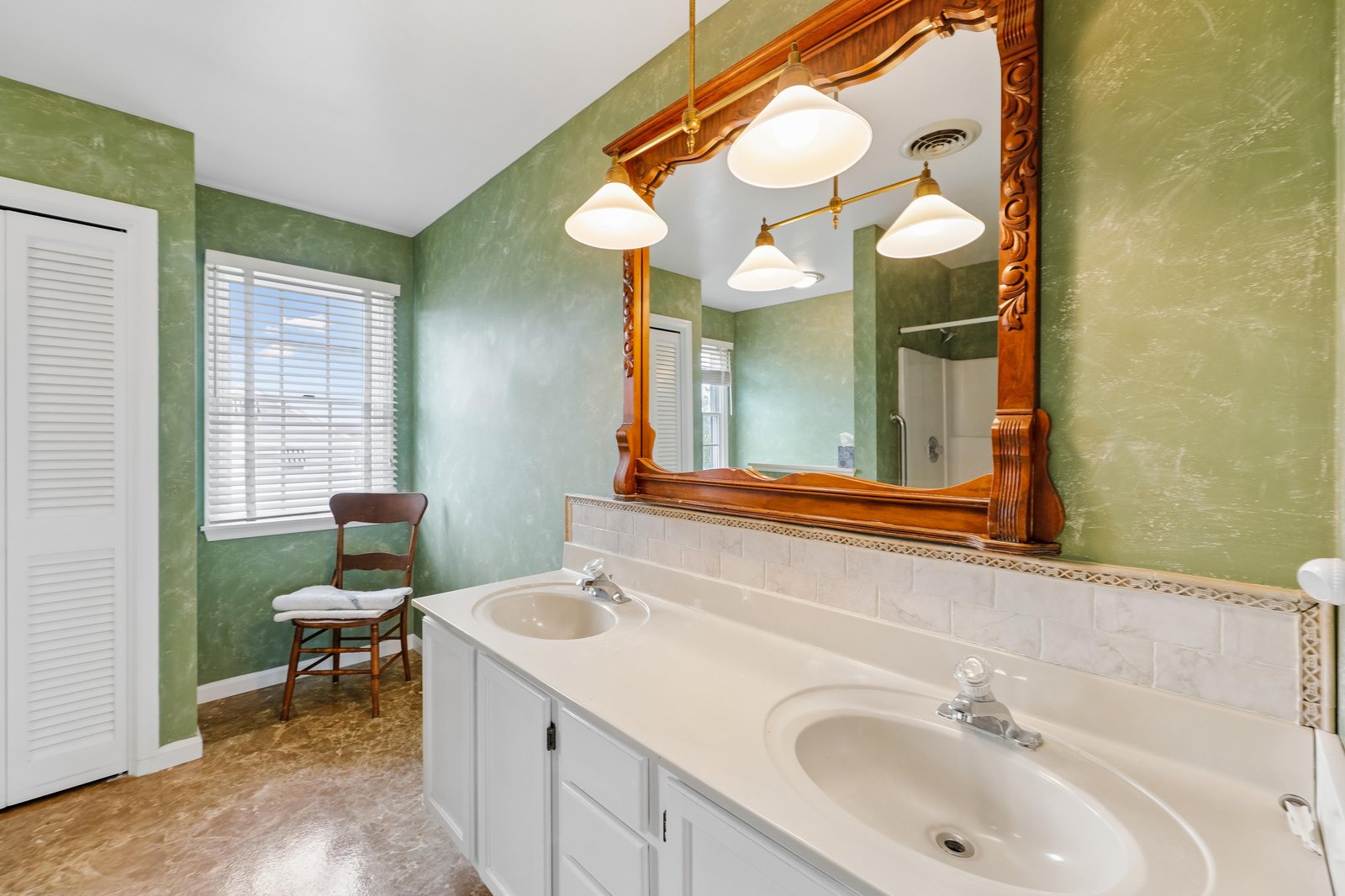 Freshen up in your spacious bathroom with charming green walls, dual sinks, and a gorgeous ornate wooden mirror that adds character to your daily routine.