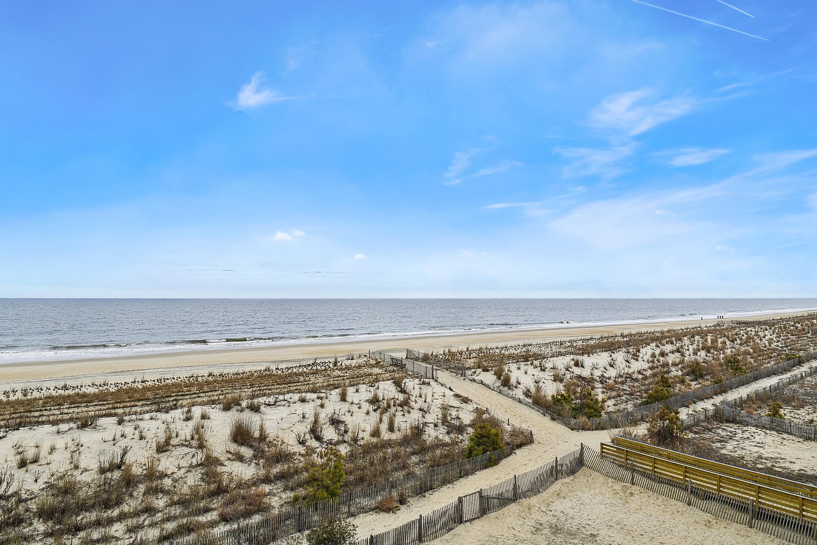 A scenic boardwalk leads directly from the property to a wide, uncrowded beach where gentle waves meet soft sand under an endless blue sky.