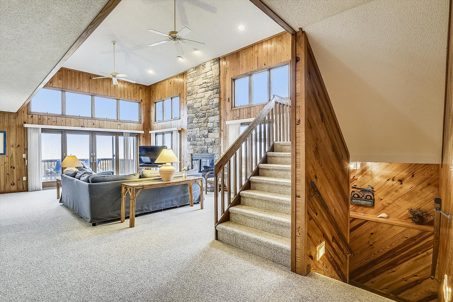 Warm wood beams and soaring ceilings create an inviting mountain retreat. Natural light floods through expansive windows, illuminating the cozy living space and stunning stone fireplace.