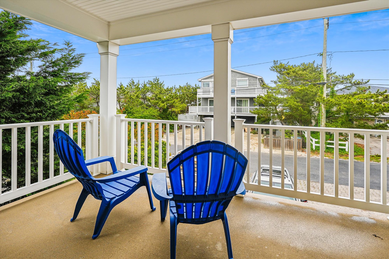 This covered balcony with cheerful blue chairs overlooks a peaceful residential neighborhood, providing a comfortable outdoor retreat during your stay.