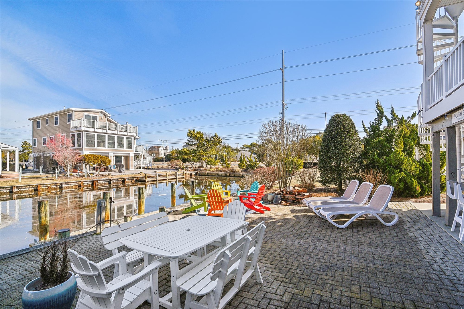 Waterfront paradise with your private dock, colorful Adirondack chairs, and sunny loungers perfect for morning coffee or sunset cocktails by the canal.