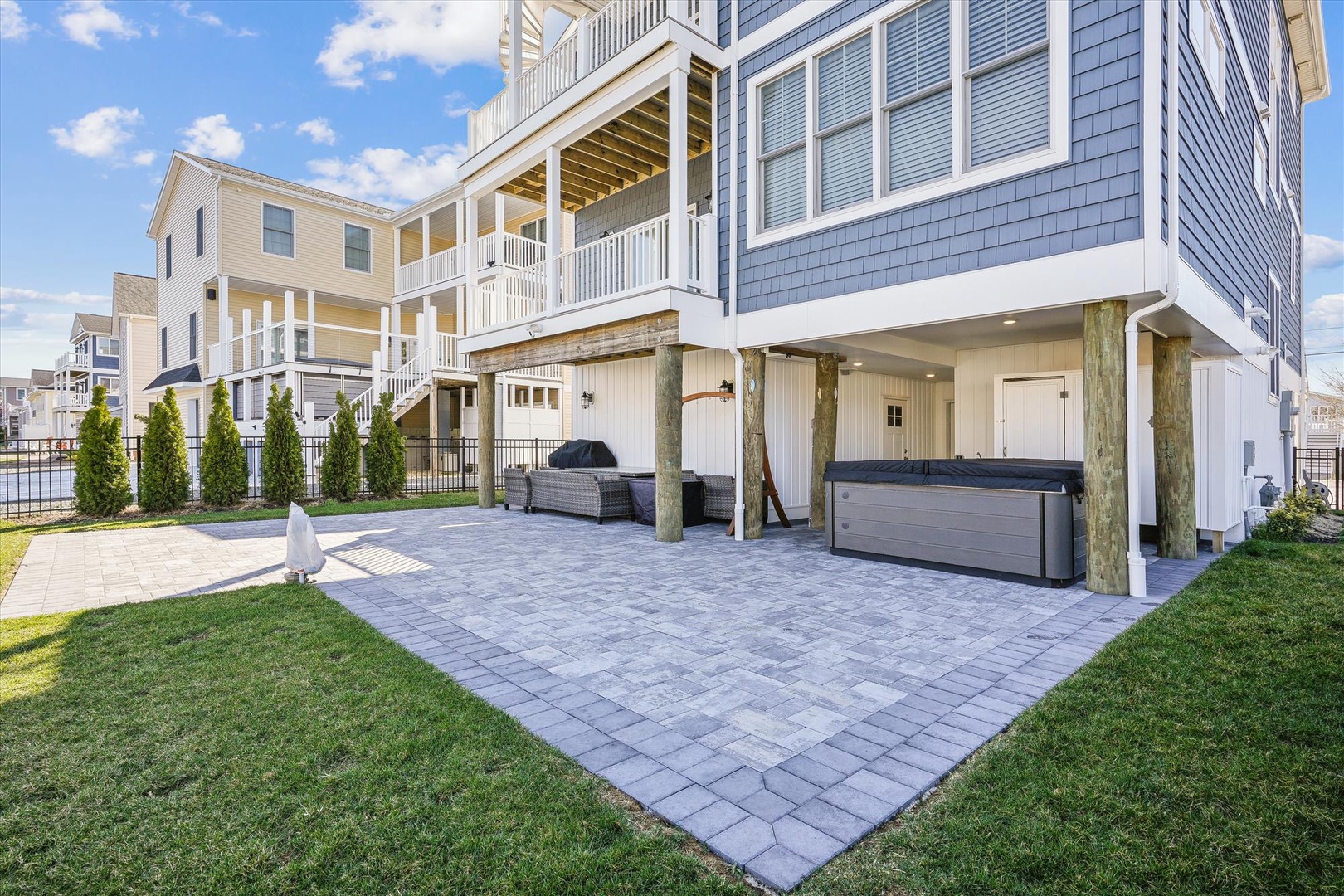 Spacious paved patio features hot tub and outdoor seating, perfect for relaxing after beach days with manicured lawn surrounding.