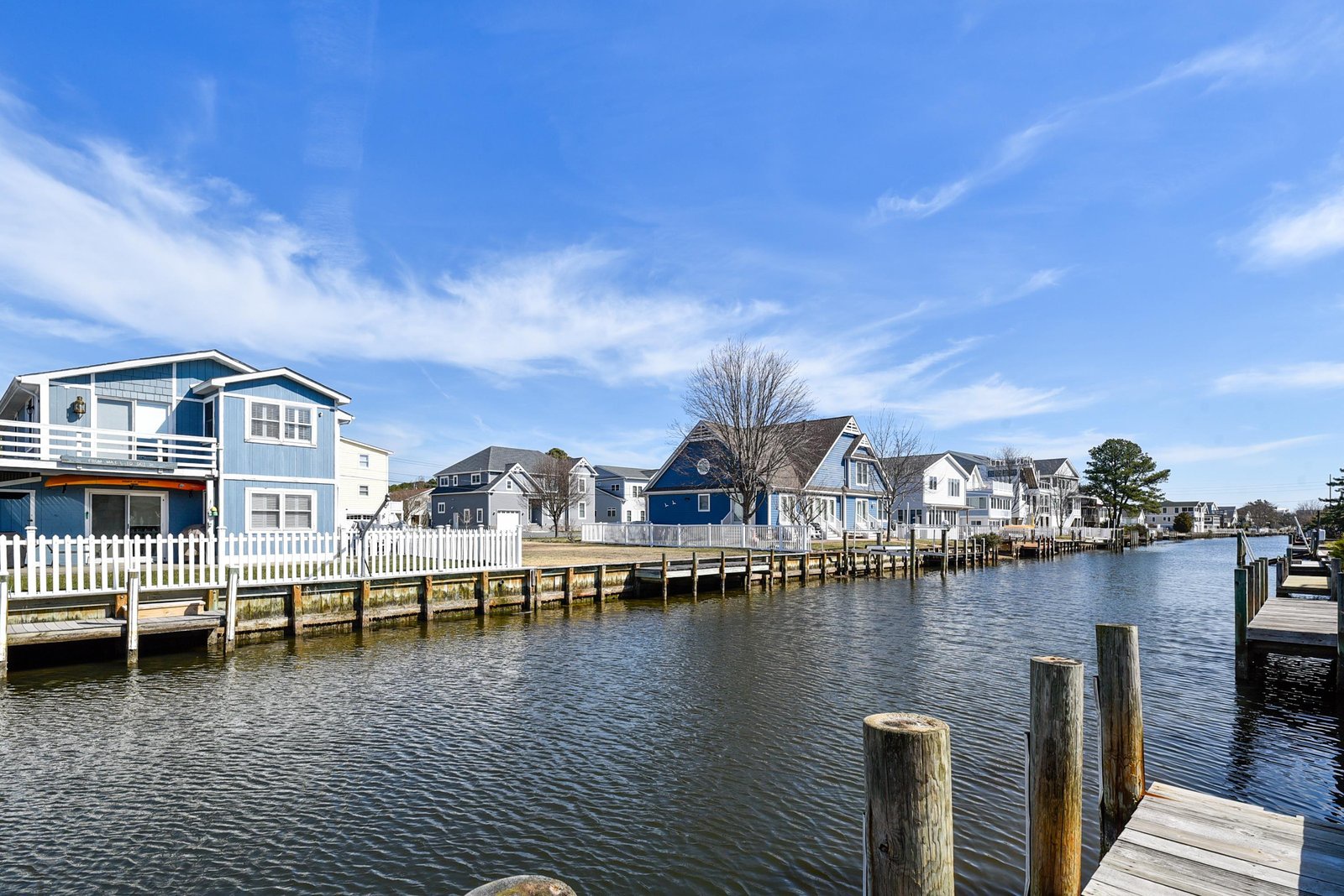 A serene waterfront neighborhood with private docks and charming coastal homes lining the peaceful canal under a bright blue sky.