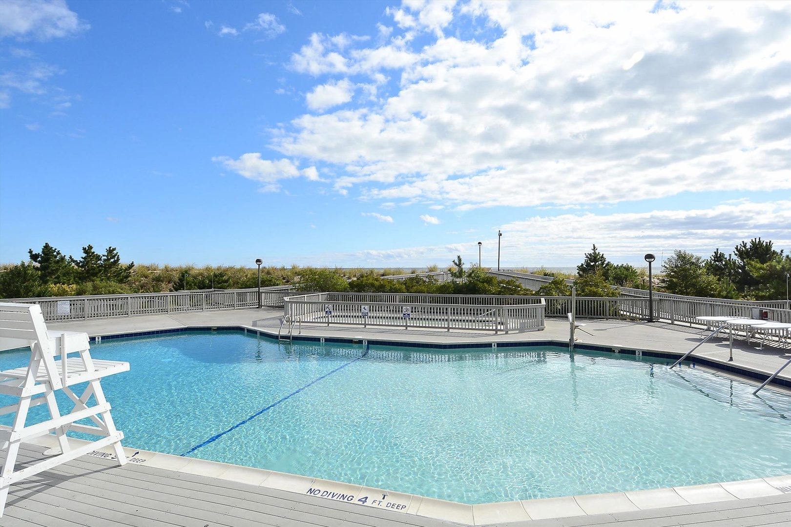 Outdoor pool deck with sunny skies, surrounded by coastal dunes and native greenery—a peaceful spot for relaxation and ocean breezes.