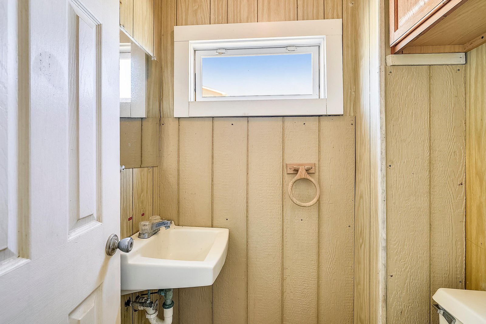 A cozy bathroom features natural wood paneling and a small window letting in soft daylight. Simple yet functional, this space provides everything you need for your stay.
