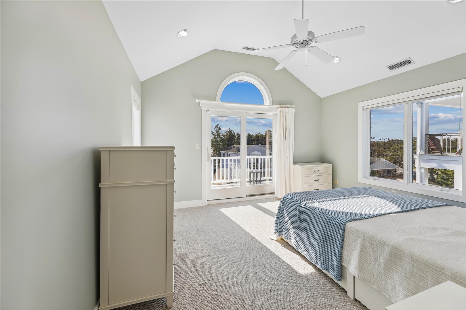 Wake up to natural light flooding your serene bedroom. The vaulted ceiling and arched window create an airy, coastal atmosphere, while balcony doors invite you to step outside and savor refreshing breezes.