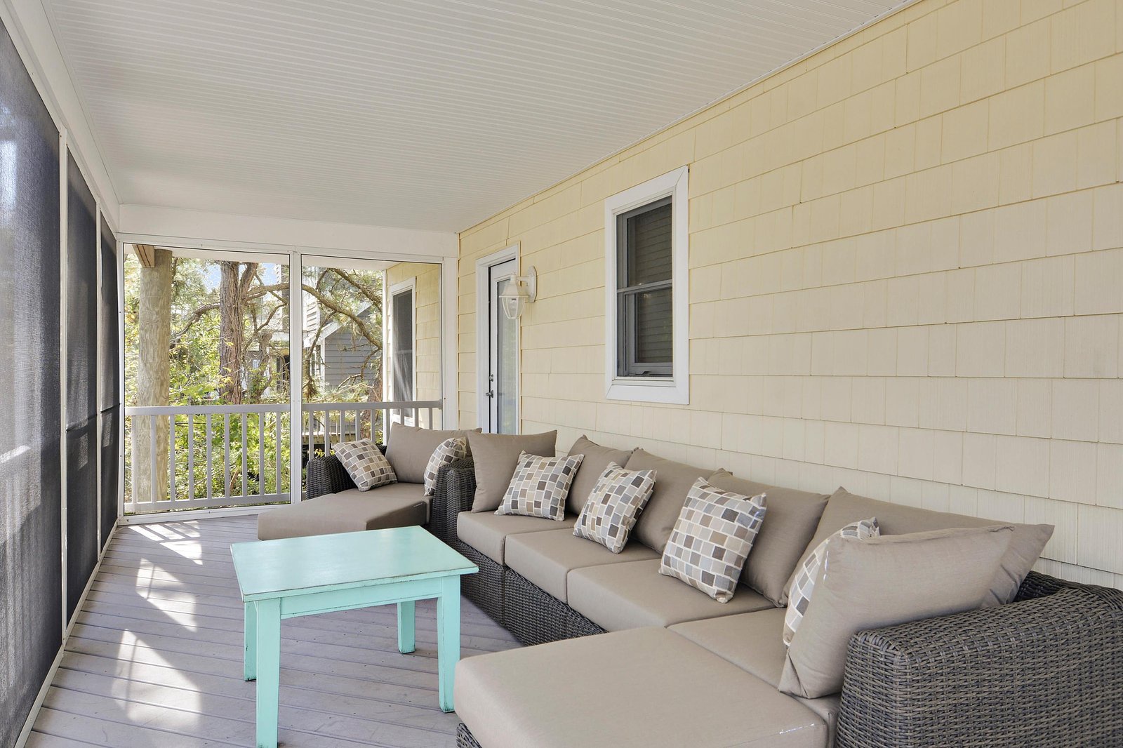 Relax on your screened porch with comfortable seating, shaded from the sun while enjoying glimpses of greenery beyond the railing.