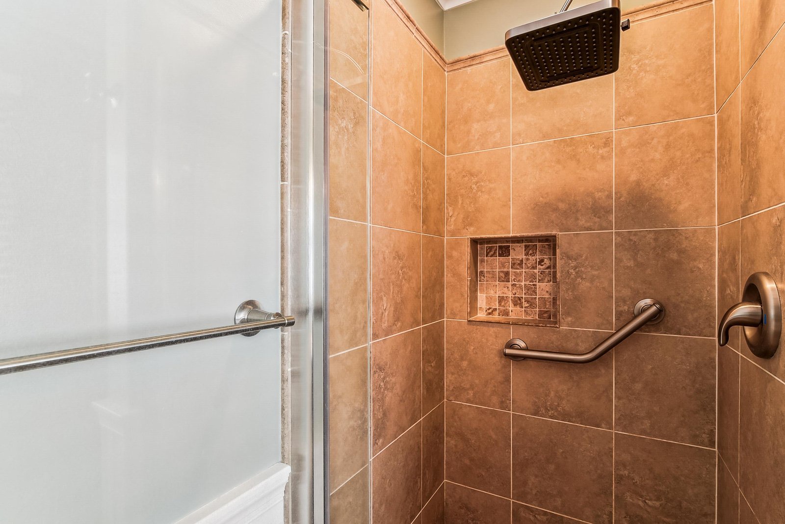 Step into your spacious walk-in shower with warm terracotta tile, rainfall showerhead, and built-in grab bars—a blend of comfort, safety, and relaxation.