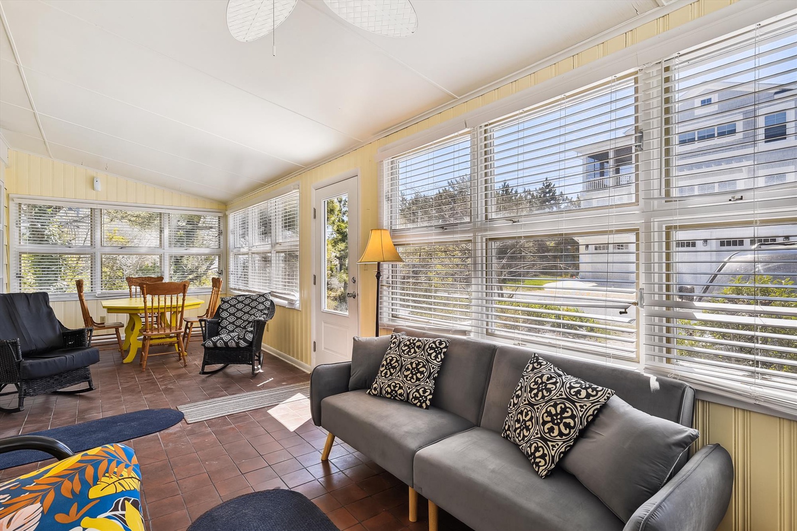 Bright sunroom with comfortable seating and dining table, perfect for morning coffee while enjoying neighborhood views through walls of windows.
