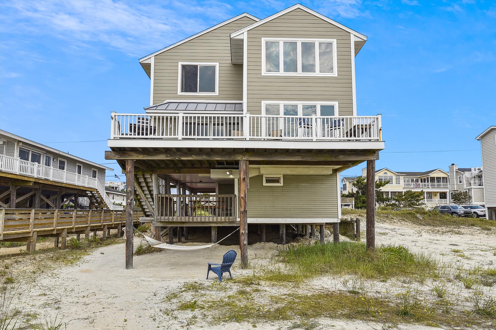 A two-story beachfront vacation home elevated on stilts, featuring a spacious wrap-around deck and direct beach access in a coastal residential area.