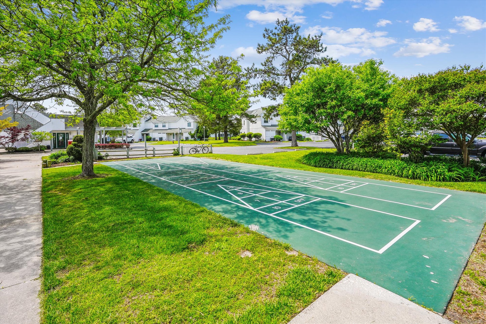 Outdoor shuffleboard court surrounded by lush gardens and mature trees in a peaceful residential setting.