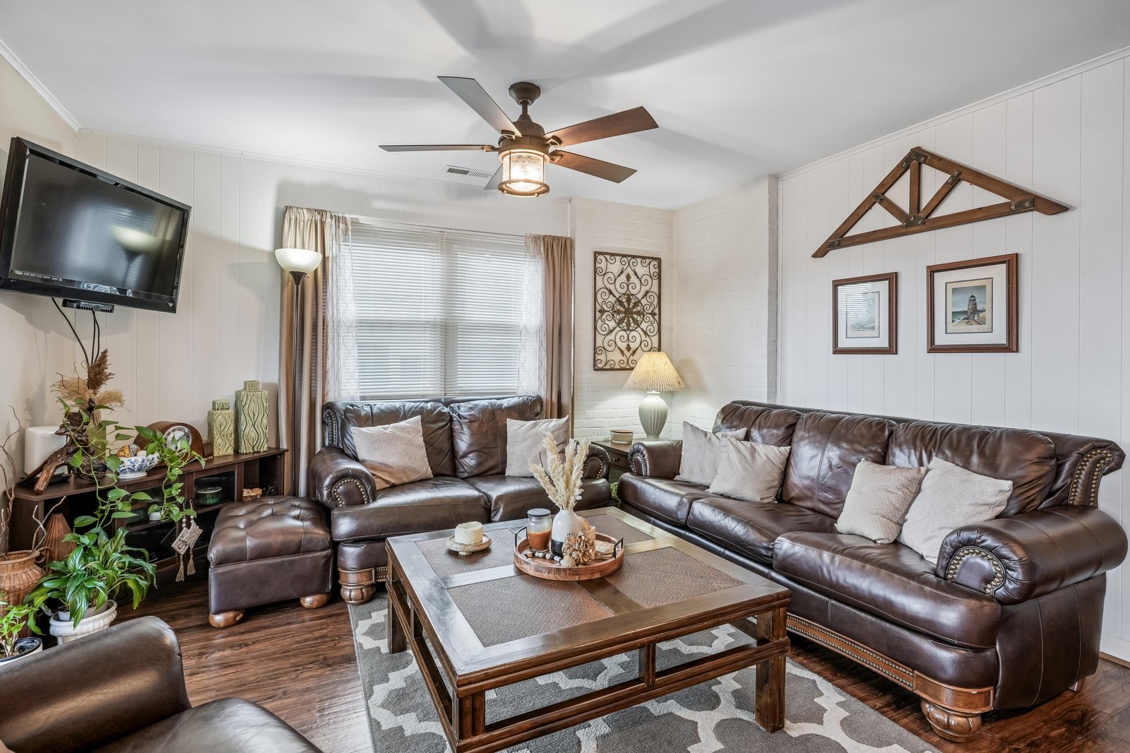 Sink into rich leather sofas where rustic charm meets modern comfort—your perfect spot to unwind with loved ones under the warm glow of the ceiling fan.