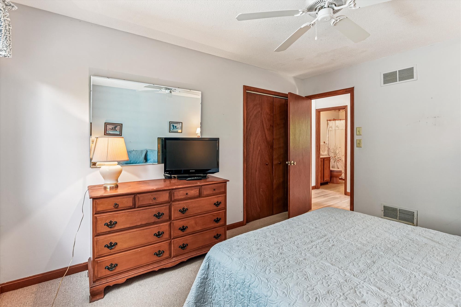 Unwind in your comfortable bedroom featuring a cozy ceiling fan, entertainment center, and beautiful wood furnishings for a relaxing stay.