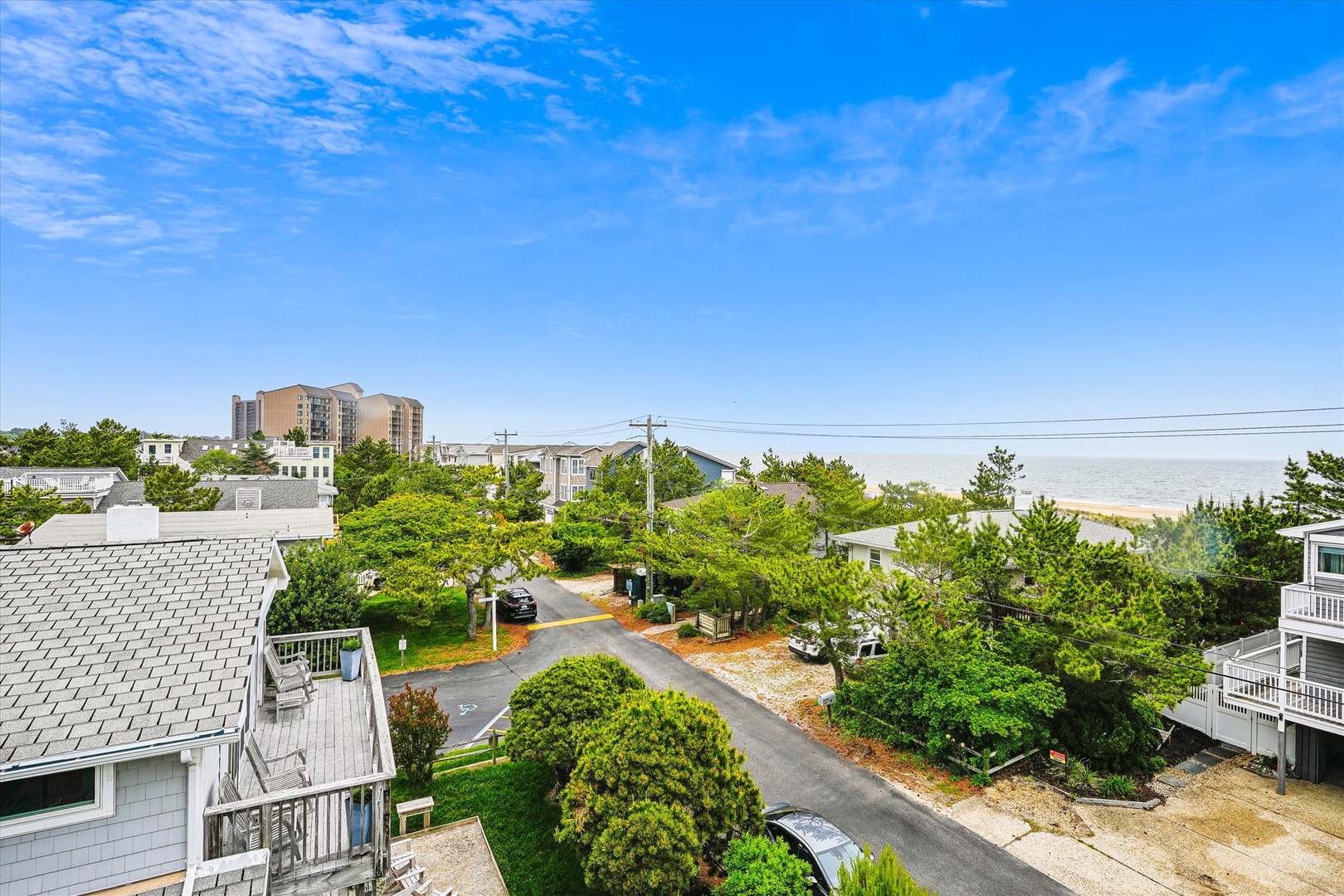 Elevated neighborhood view showcasing a coastal residential area with beach access, surrounded by lush greenery and nearby buildings under a bright blue sky.