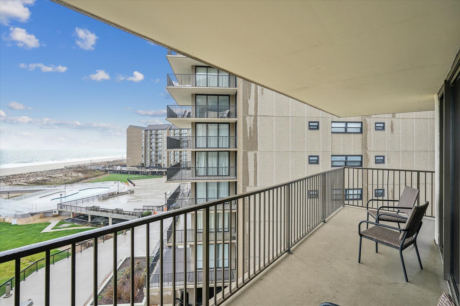 The balcony offers direct views of the nearby property buildings and beach area, with a pool complex visible from this elevated perspective at the vacation rental property.