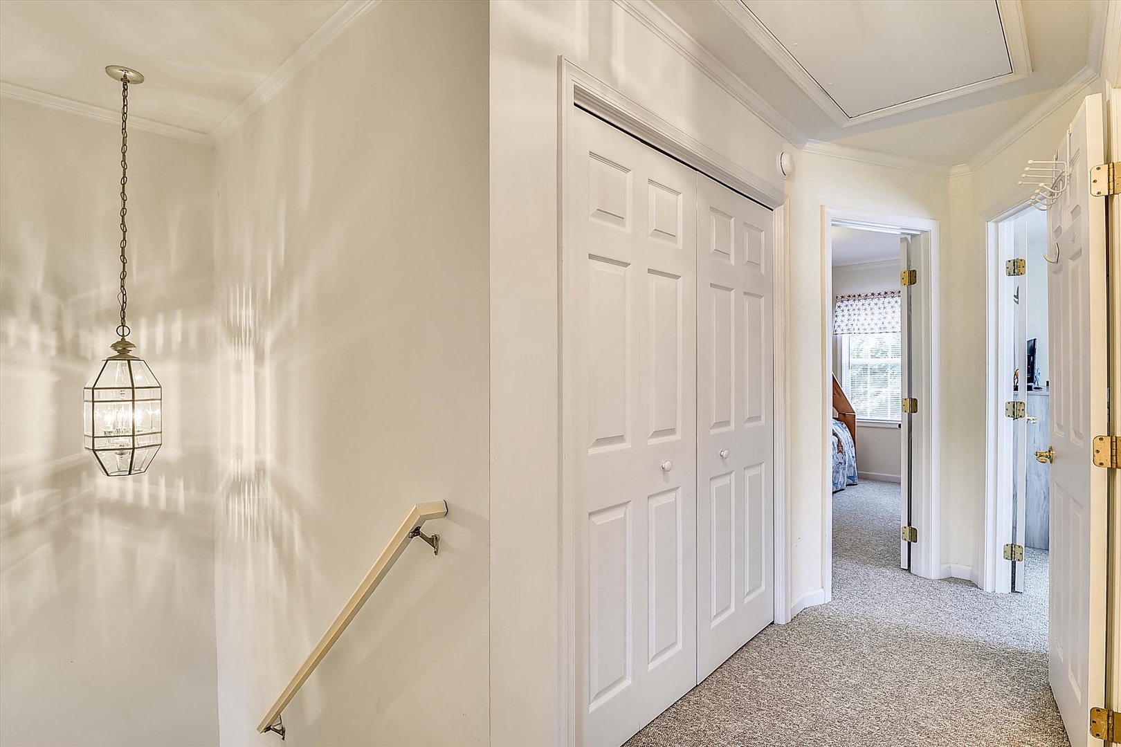 A bright hallway with charming pendant lighting connects the bedroom spaces, offering plenty of storage with built-in closets and a glimpse of cozy rooms beyond.