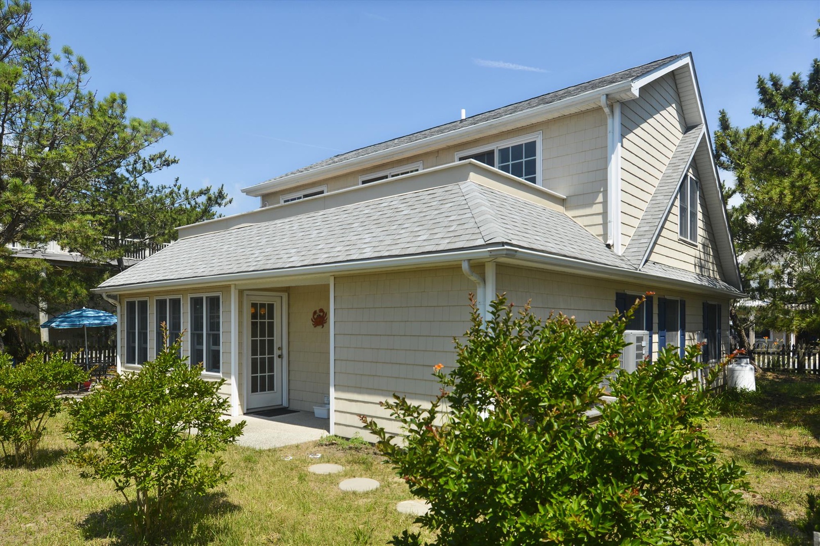 A charming coastal home with distinctive architectural details, surrounded by mature landscaping and nestled among tall pines, creating a peaceful private setting in a welcoming neighborhood.