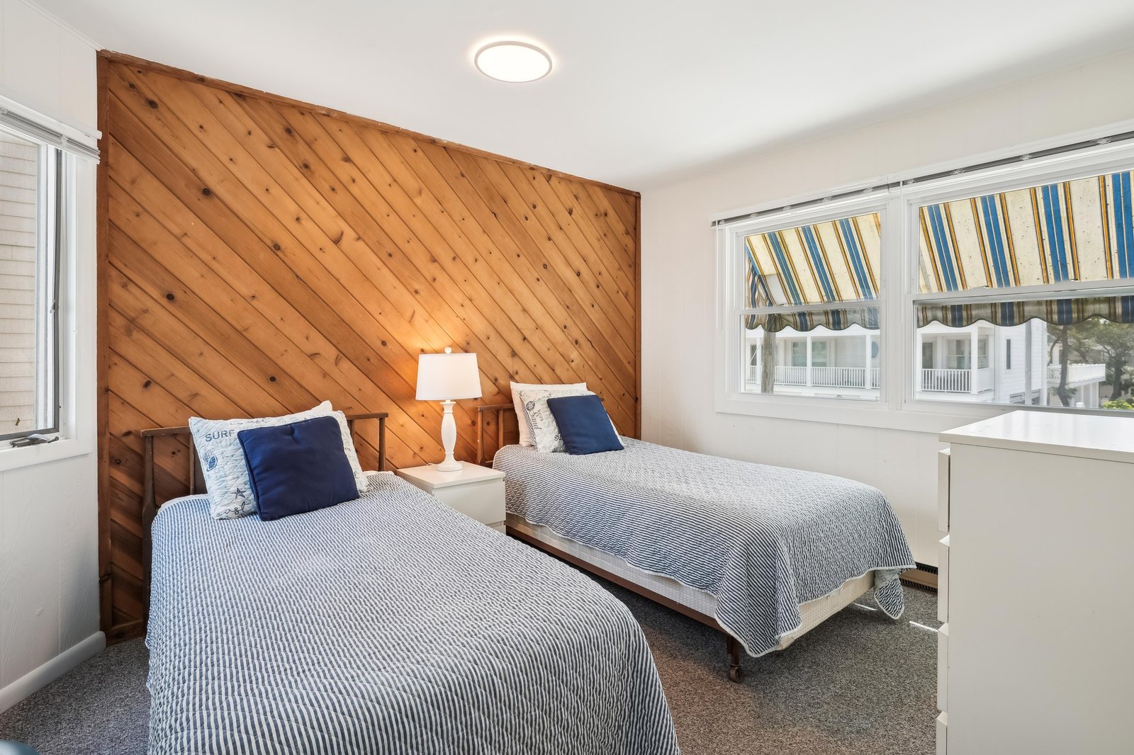 Your cozy coastal retreat features twin beds dressed in soft blue linens, framed by a striking diagonal wood accent wall that brings warmth and character to your restful space.