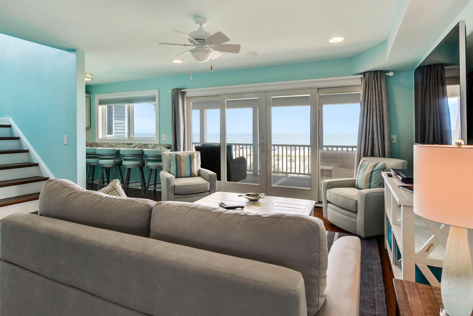 Relax in your bright, coastal living space with sweeping ocean views through the glass doors, where the gentle ceiling fan and turquoise accents create a soothing seaside vibe.