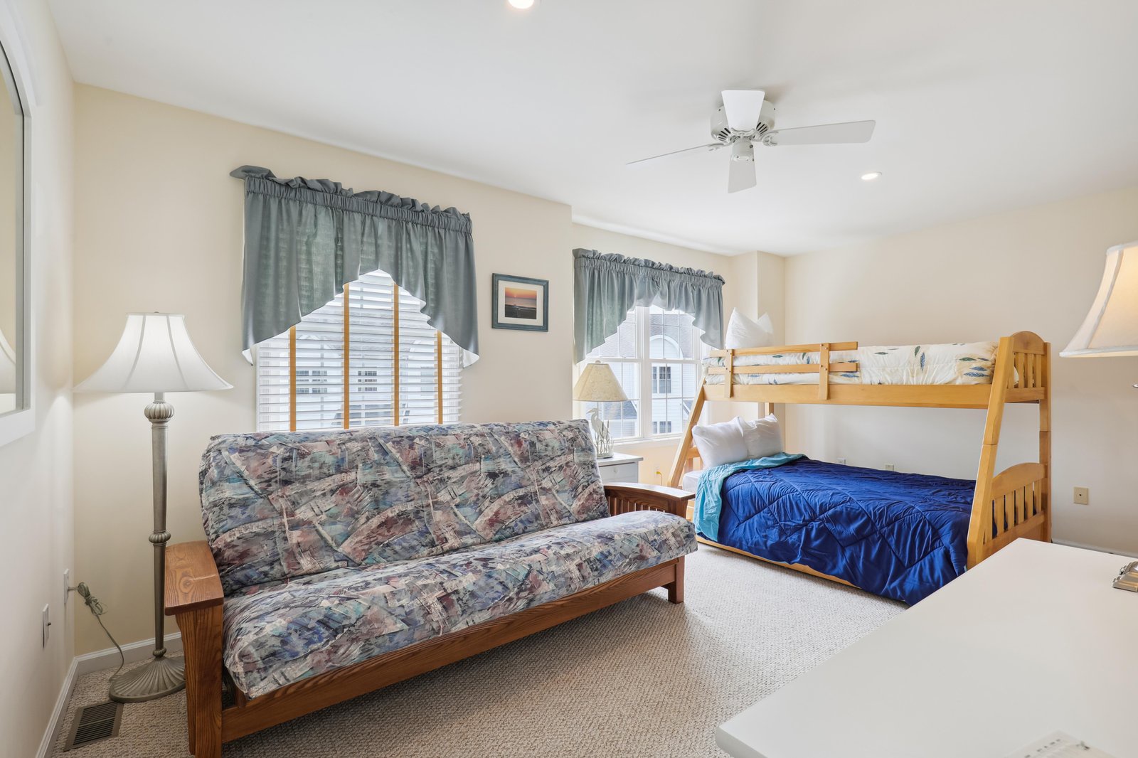 Relax in your comfortable space with a cozy futon and sturdy bunk bed, perfect for families. Soft lamps, a gentle ceiling fan, and charming curtains create a warm, inviting atmosphere.