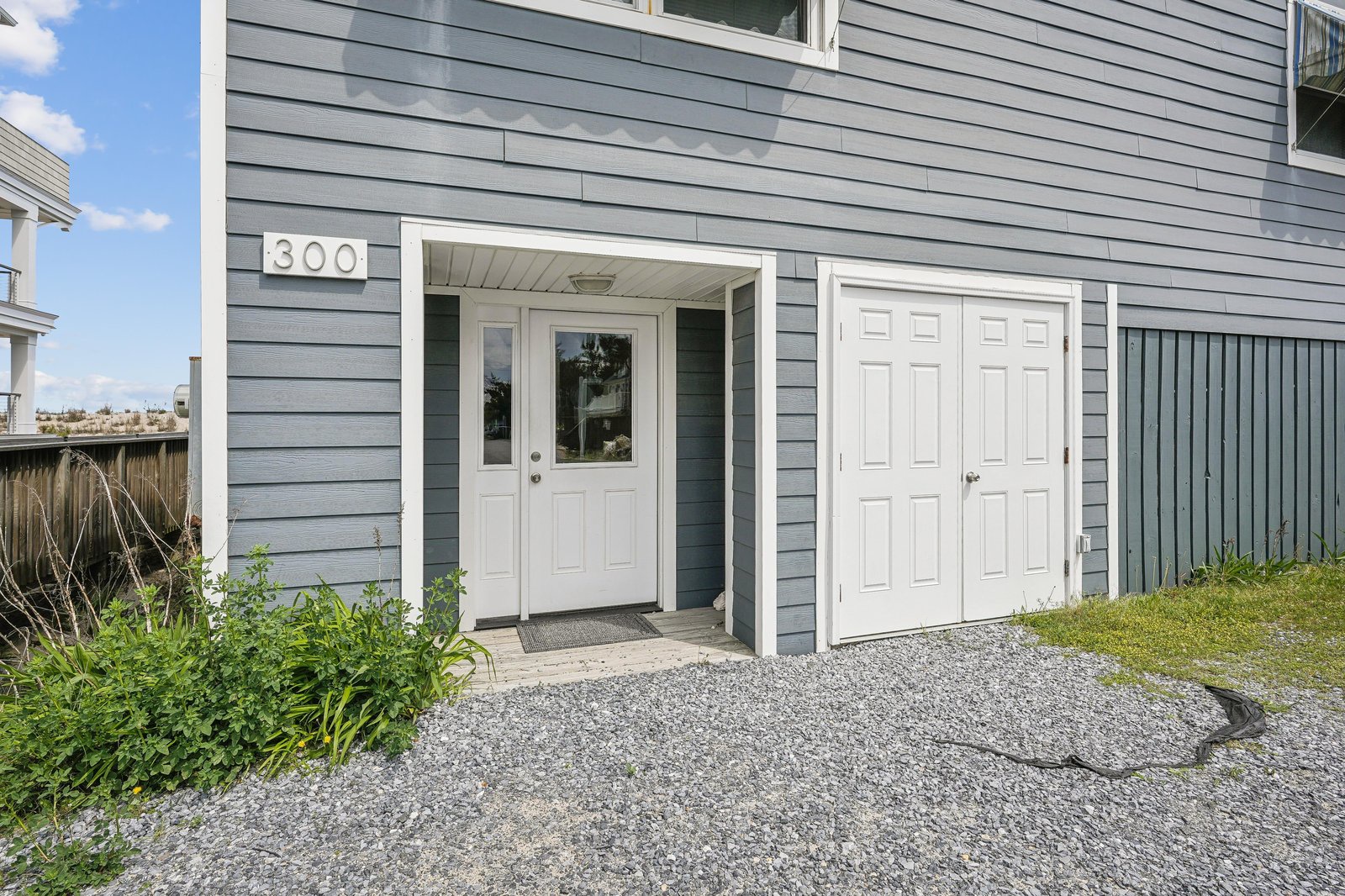 Unit 300 welcomes you with its crisp gray exterior, white doors, and covered entryway set on a clean gravel path surrounded by greenery.