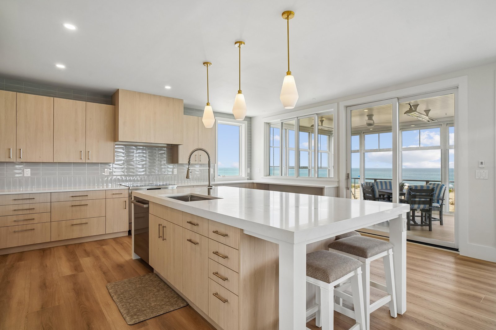 Your modern kitchen blends soft wood tones with a sleek quartz island and elegant pendant lights, while glass doors invite you outside to enjoy sweeping ocean views right from the terrace.