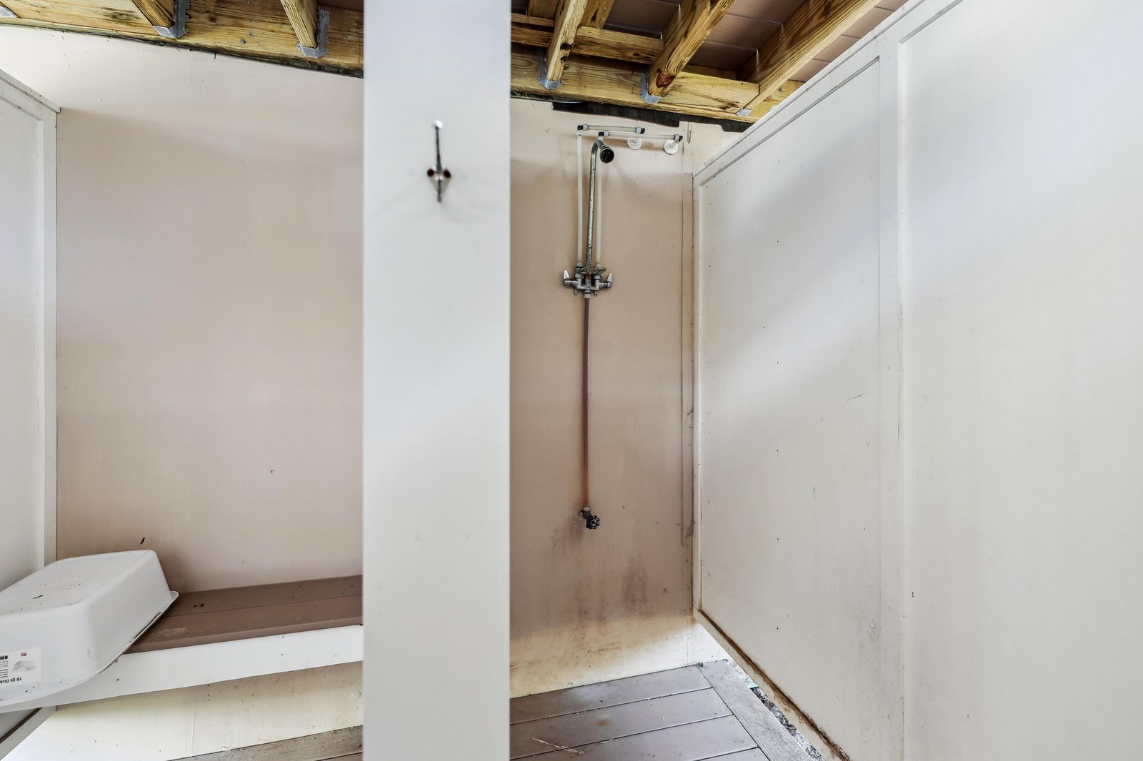 A minimalist shower space with rustic wood-beam ceiling and concrete walls invites you to rinse off after exploring your coastal retreat.