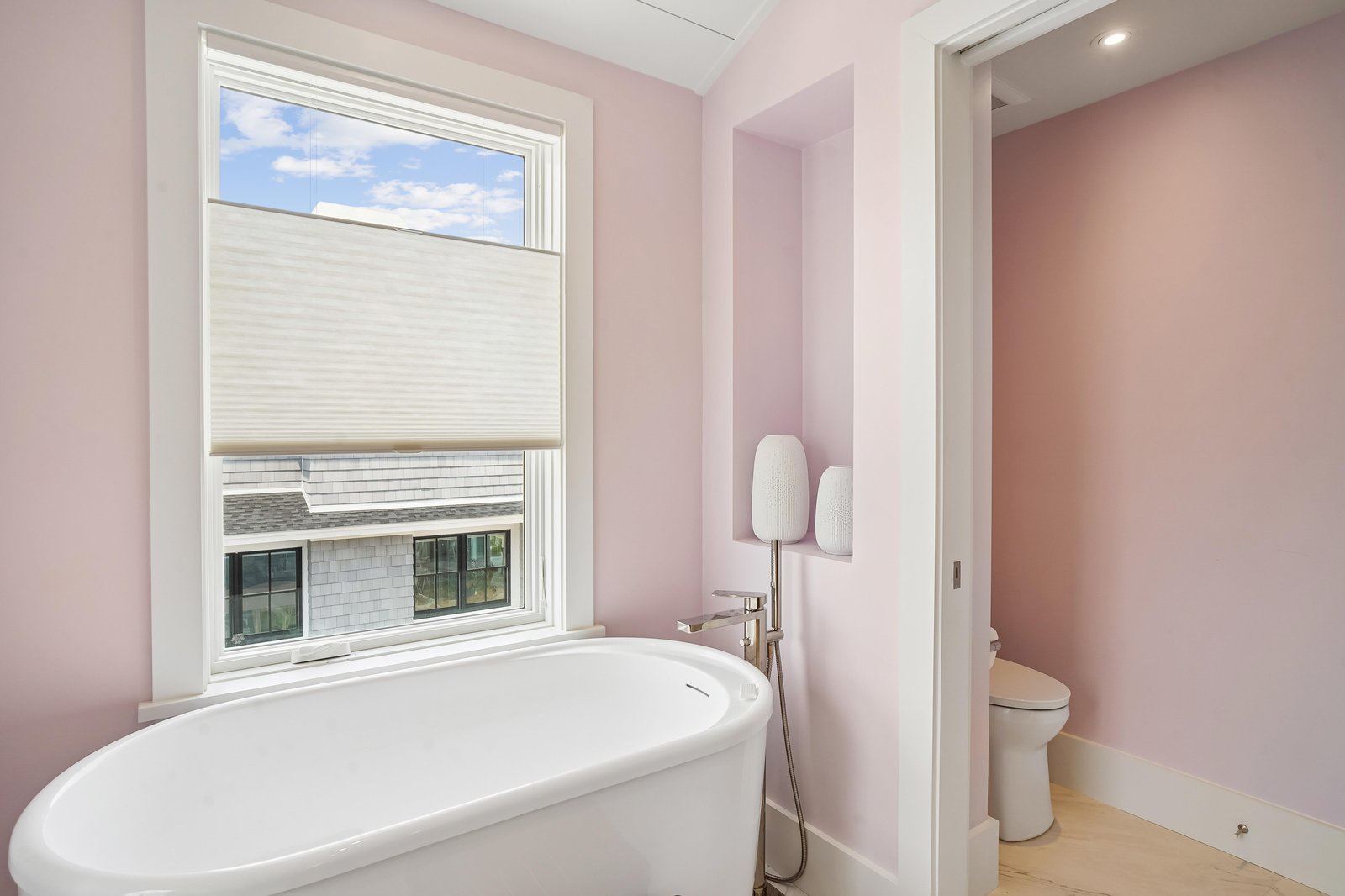 Sink into the freestanding soaking tub in your serene pink bathroom, where soft natural light and modern fixtures create a spa-like retreat for relaxation.