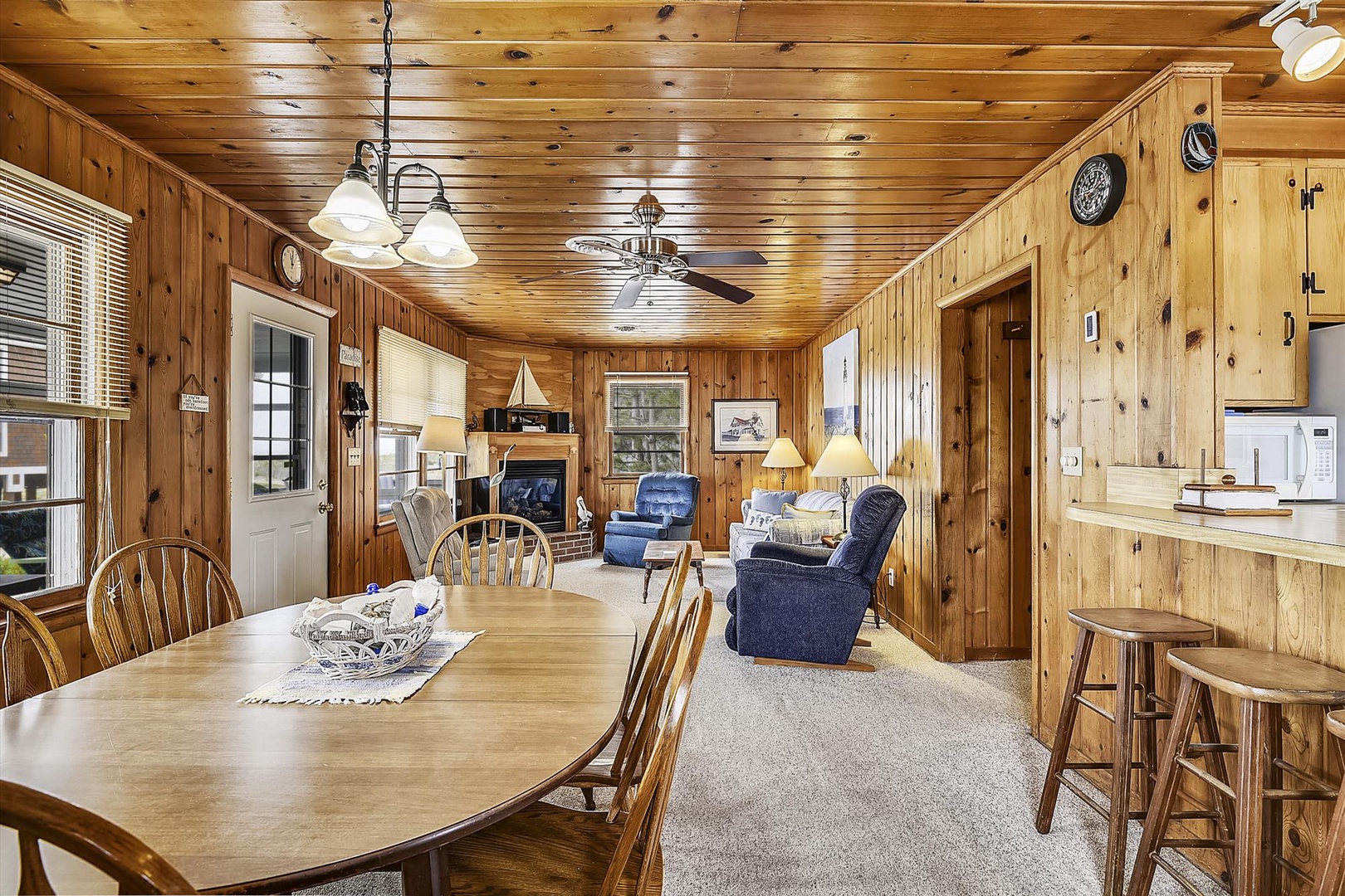 Step into your cozy cabin retreat with warm pine walls, a welcoming dining table, and plush recliners by the fireplace—your perfect home away from home.