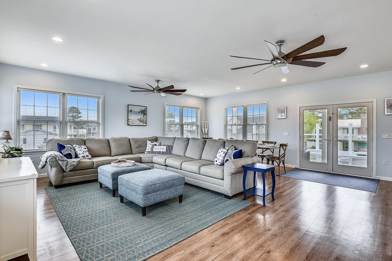 Settle into your spacious living room with plush sectional seating, gentle ceiling fans, and natural light streaming through generous windows that frame peaceful neighborhood views.