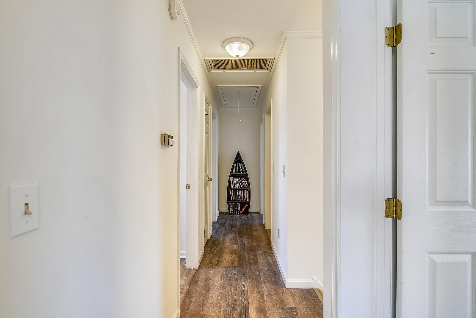 Bright hallway with warm wood-style flooring leads you to your private spaces, with a charming boat-shaped bookshelf adding a nautical touch at the end.