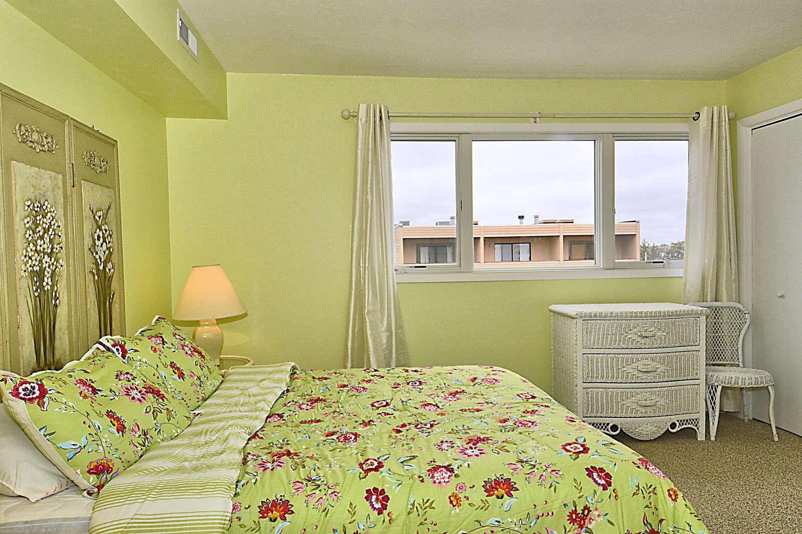 Bright and cheerful, this sunny bedroom invites you to unwind with playful floral bedding, wicker accents, and soft natural light streaming through white curtains.