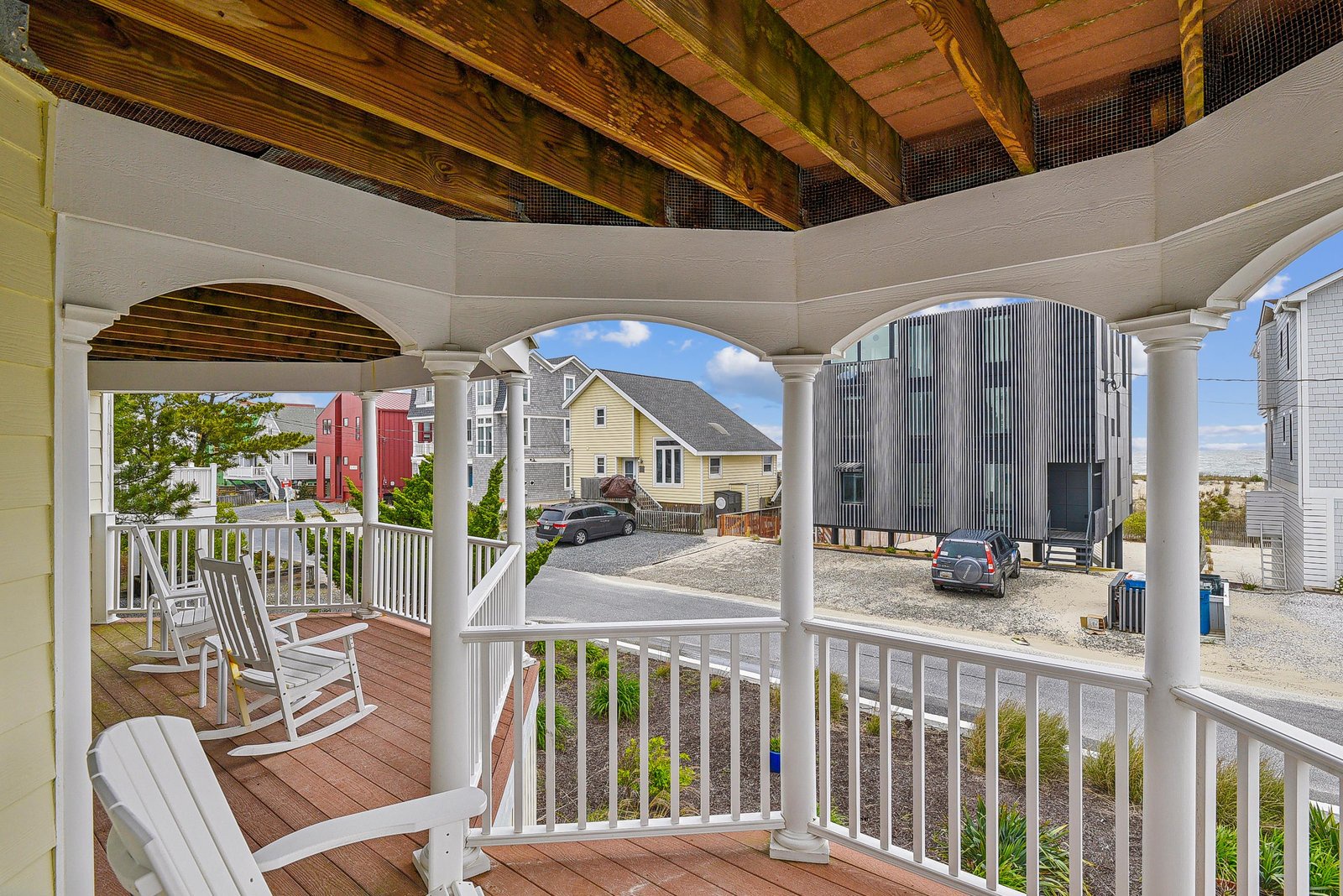 Classic covered porch with white columns and railings, featuring a rocking chair perfect for relaxing. Exposed wooden beams add rustic charm to this breezy coastal retreat.