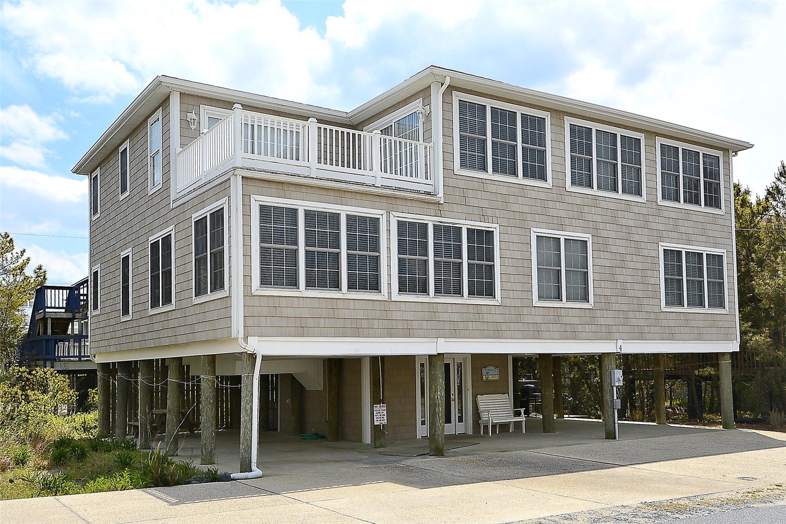 This elevated coastal-style home features natural wood siding, expansive windows, and upper-level balconies overlooking the surrounding landscape, with covered parking on the ground level.
