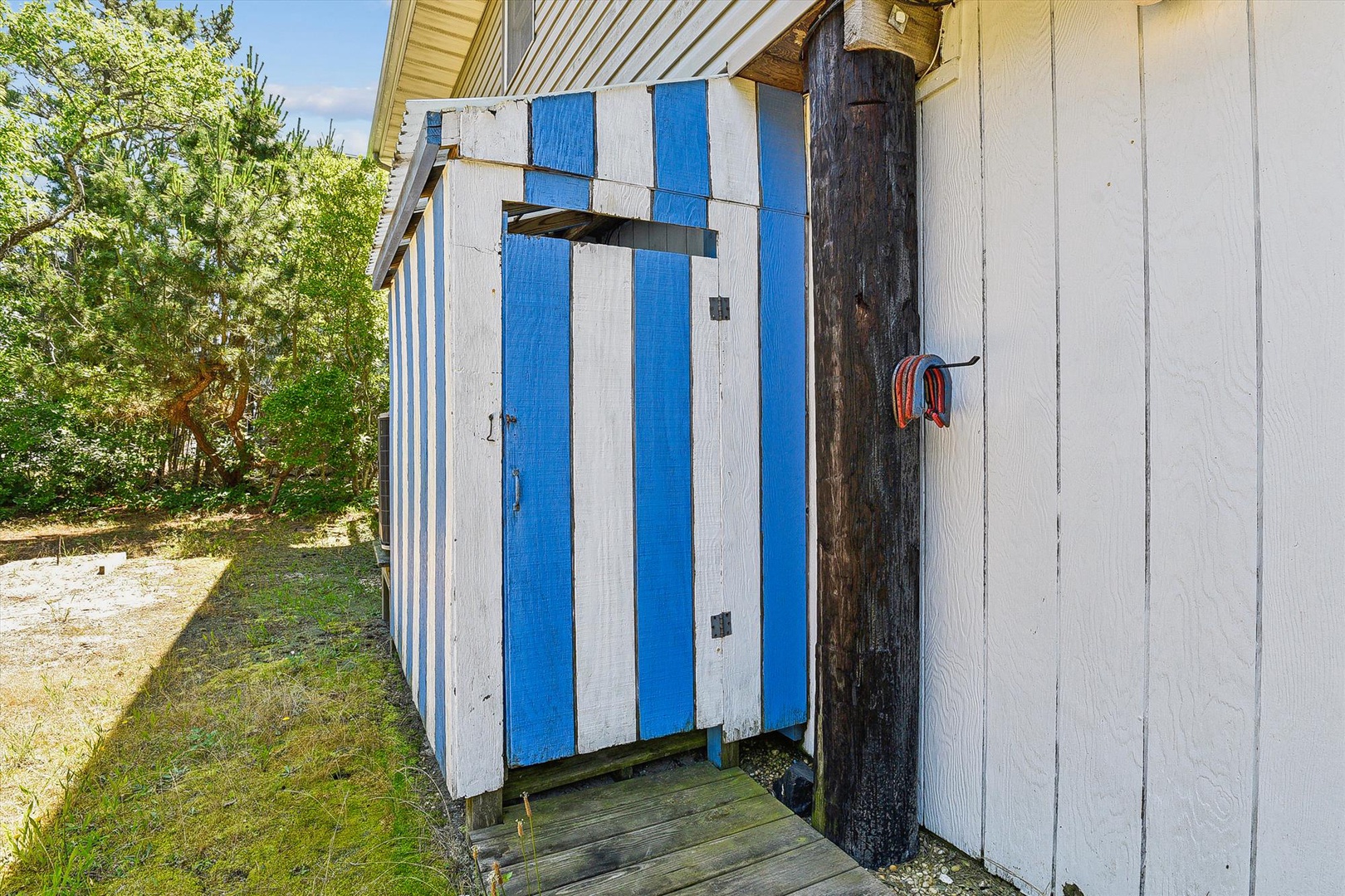 Charming blue-and-white striped outdoor shower cabin nestled among greenery—a sunny spot to rinse off after beach days or pool time at this coastal retreat.