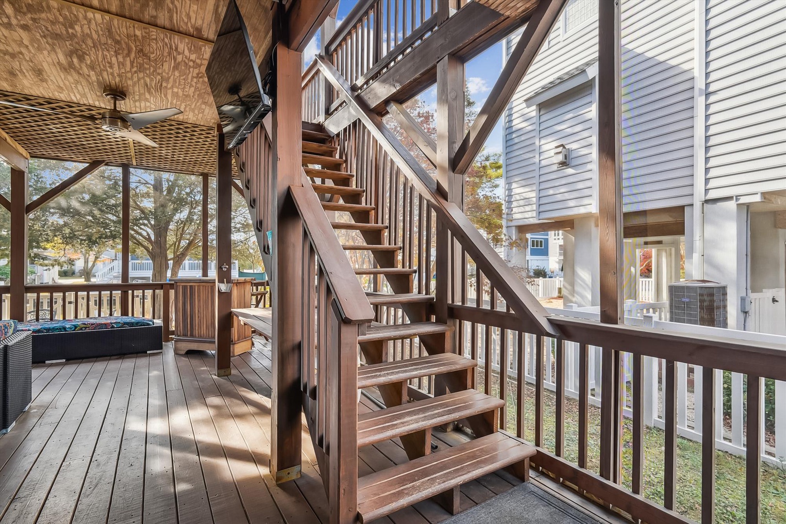 Spacious multi-level deck with open-air staircase connects indoor and outdoor living spaces, featuring comfortable seating and ceiling fans to keep you cool on warm days.