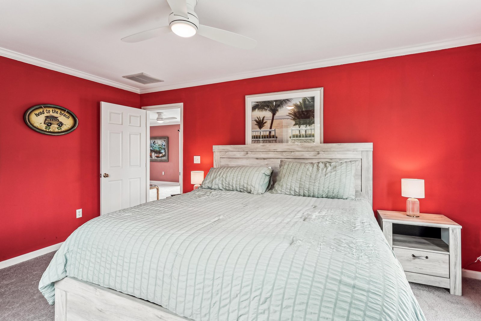 Unwind in your vibrant bedroom featuring a plush king bed, beach-inspired decor, and ceiling fan to keep you cool. Coastal artwork above the headboard and charming touches make this your perfect retreat.