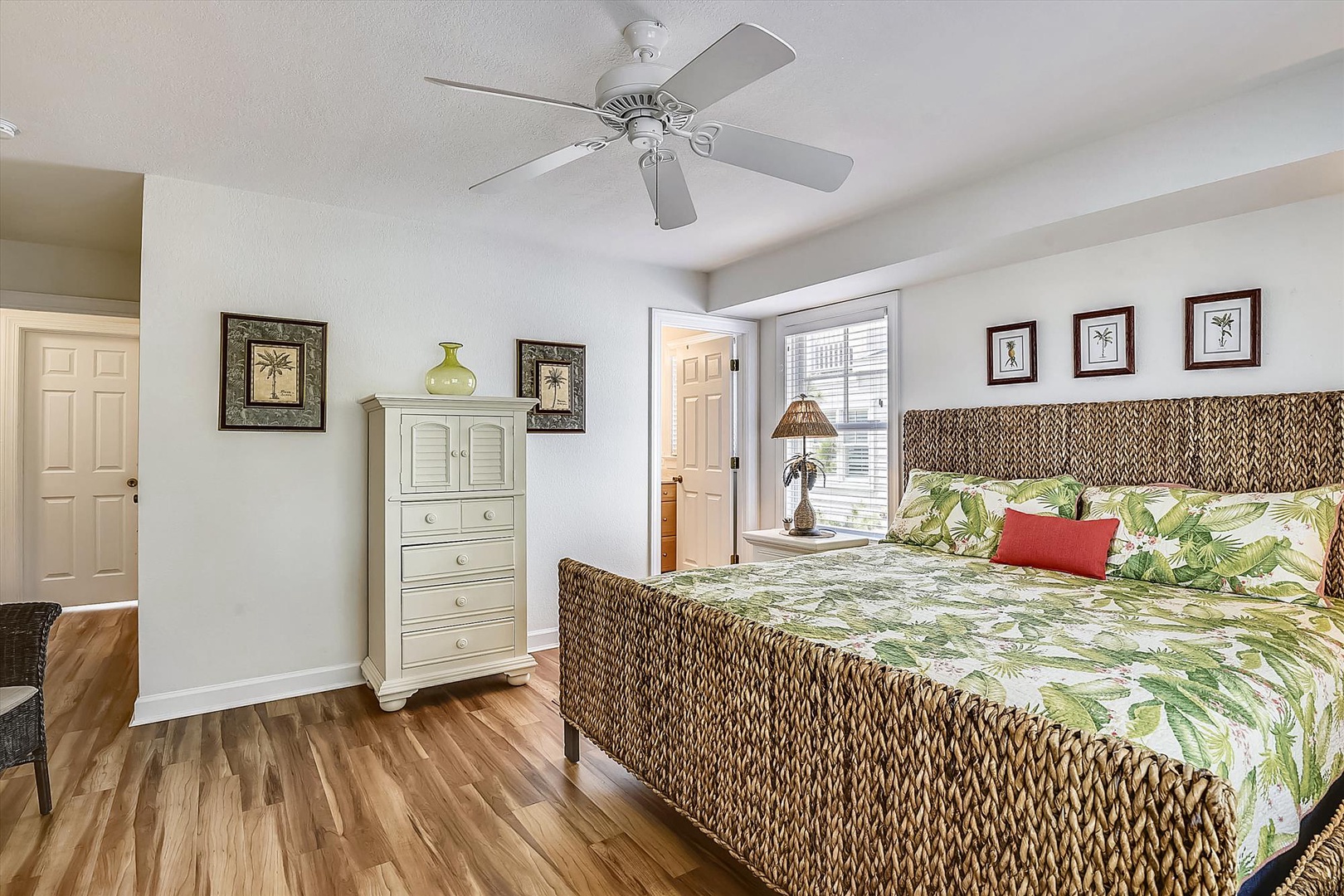 Your tropical-themed bedroom offers comfort with a ceiling fan, woven headboard, and cheerful botanical bedding for restful nights.