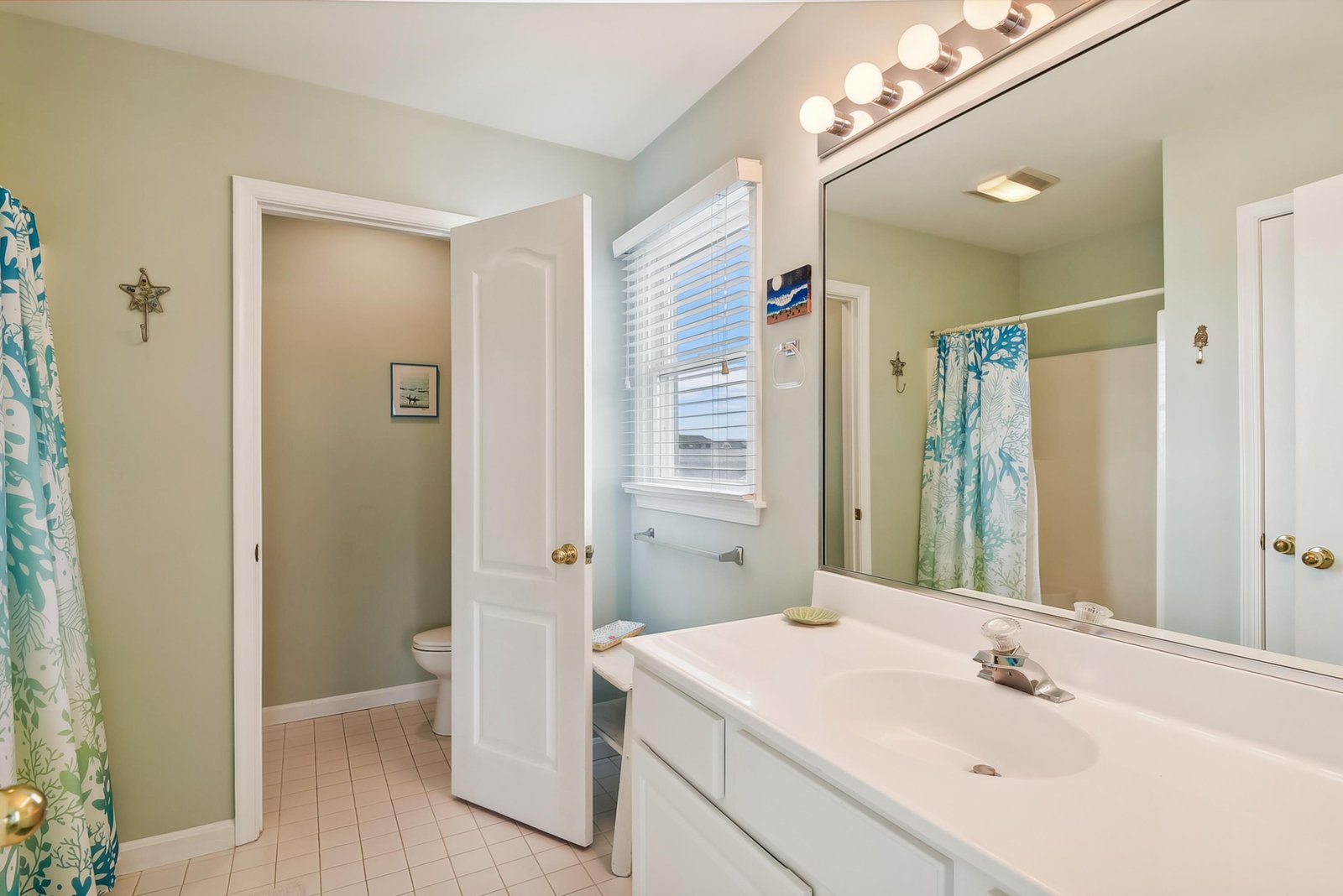 Step into your fresh, serene bathroom with coastal touches. Bright vanity lighting and a breezy window create a welcoming space to unwind and refresh each morning.