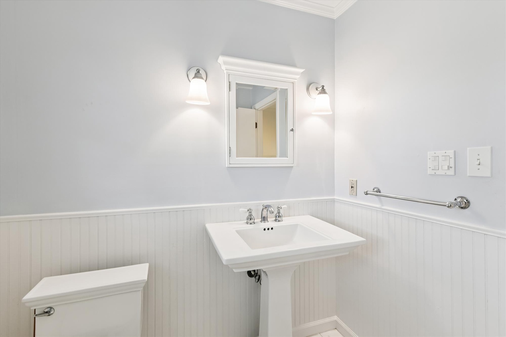 Step into your pristine powder room featuring classic beadboard wainscoting, elegant pedestal sink, and warm lighting that creates a welcoming atmosphere.