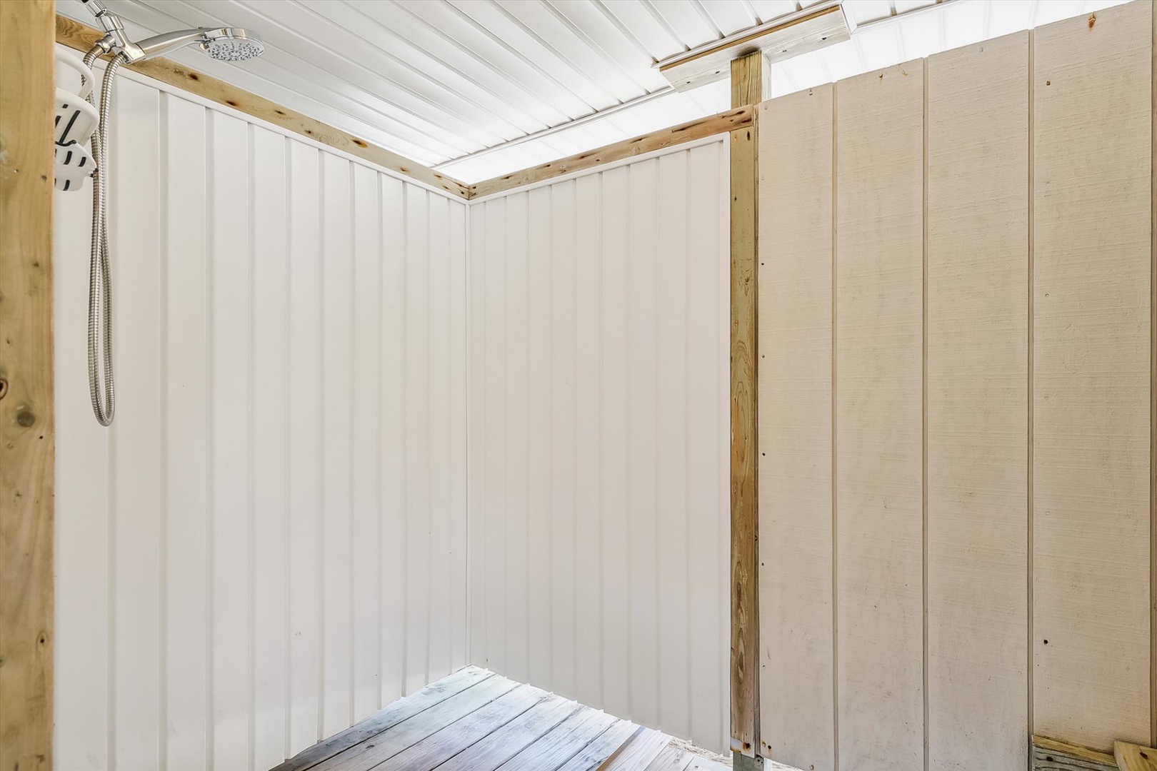 A bright outdoor shower space with fresh white walls and natural wood framing, ready to rinse off after sunny days by the pool or beach.