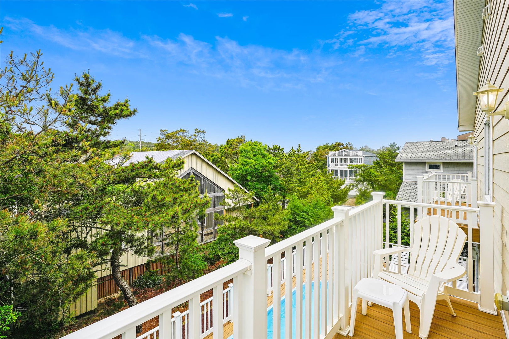 A bright balcony overlooks lush greenery and neighboring beach homes, offering a peaceful spot to enjoy your morning coffee or evening breeze surrounded by coastal charm.