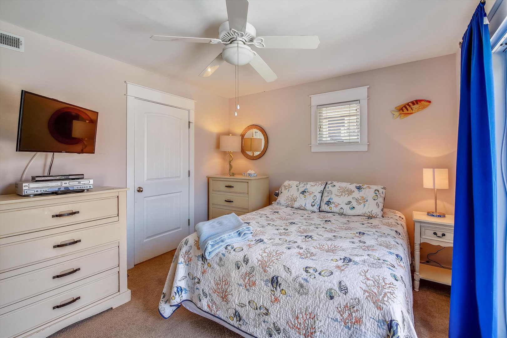 Unwind in your coastal retreat featuring a plush queen bed dressed in ocean-themed linens, modern TV and entertainment center, and gentle ceiling fan to keep you comfortable year-round.