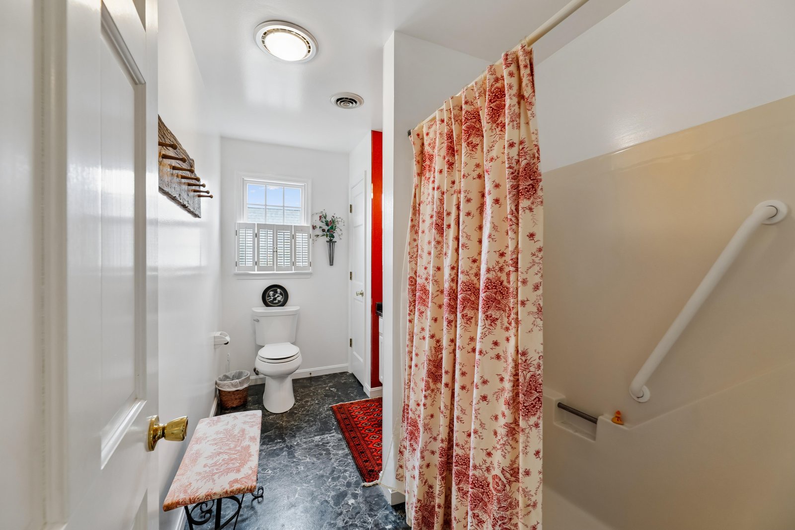 A charming bathroom awaits you with a floral shower curtain, tiled floors, and thoughtful touches like a decorative window and warm accent rugs to make your stay comfortable.