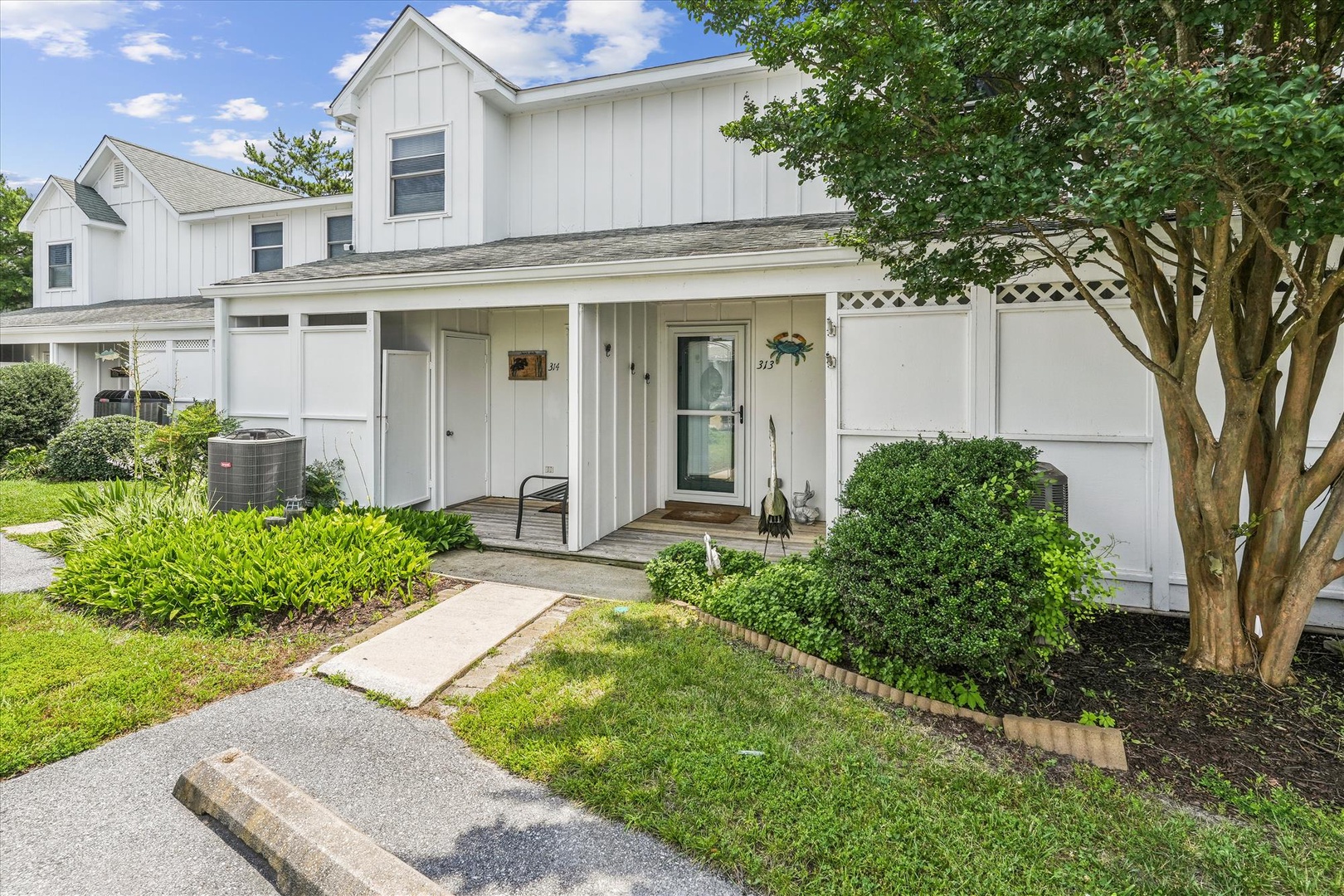 Charming white townhome with covered entrance and mature landscaping in a peaceful residential setting.