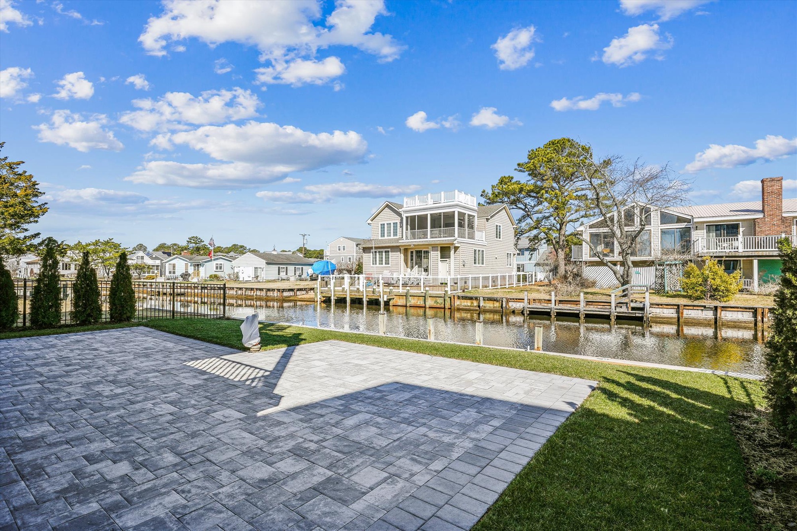 Waterfront property with private paver patio and dock access on a peaceful canal. Scenic views of surrounding coastal homes beneath a bright blue sky.