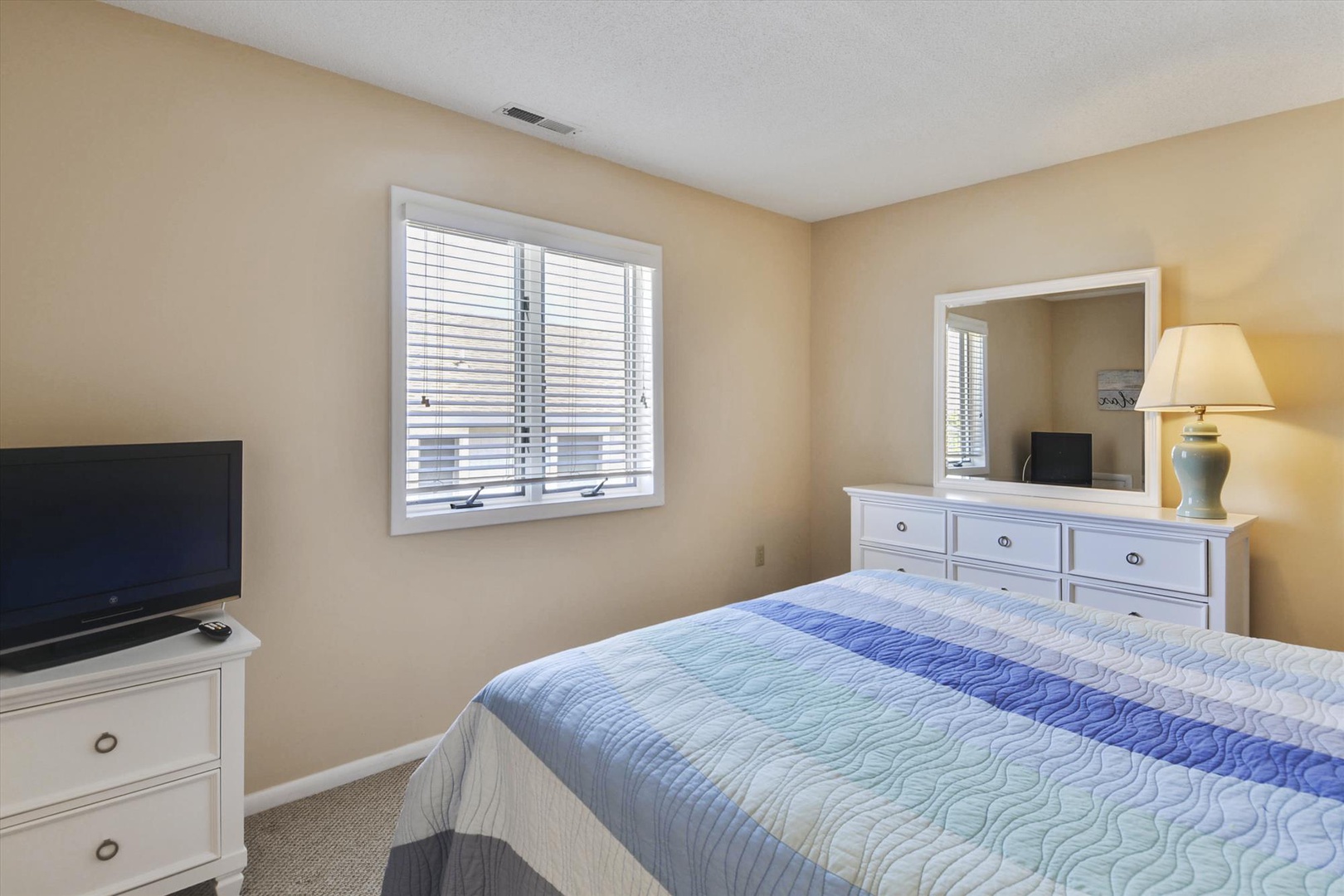 Unwind in this peaceful bedroom with a comfortable bed, fresh linens, and soft lighting. Your TV and dresser await for your convenience and relaxation.