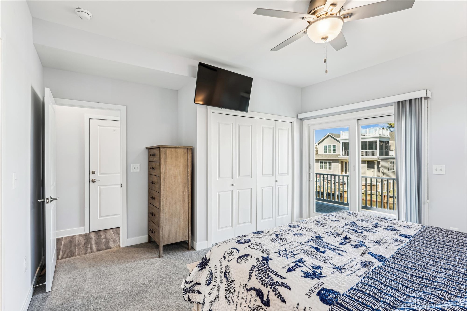 Relax in your bright bedroom with a ceiling fan, wall-mounted TV, and balcony doors opening to views of neighboring homes.