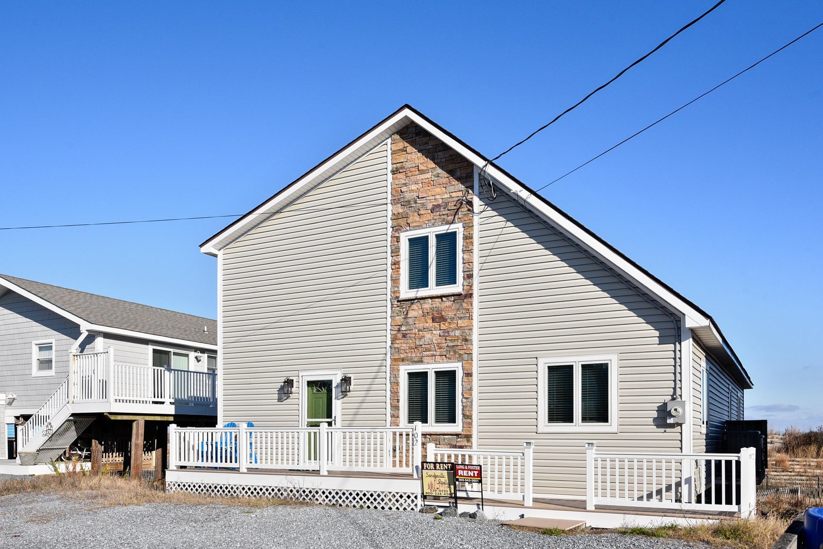 The property sits in a quiet beachside neighborhood, featuring distinctive stone accents and a welcoming front porch that marks your arrival to this coastal retreat.