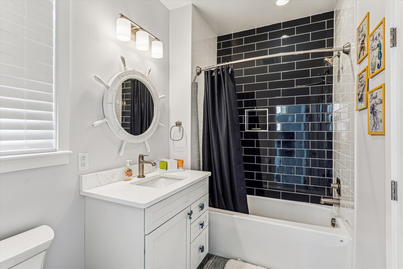 Refresh in your stylish nautical-themed bathroom, featuring a striking black subway tile shower and charming ship's wheel mirror.
